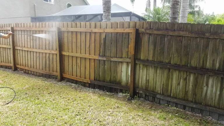 Wood privacy fence half cleaned by soft washing, showing weathered and restored boards side by side